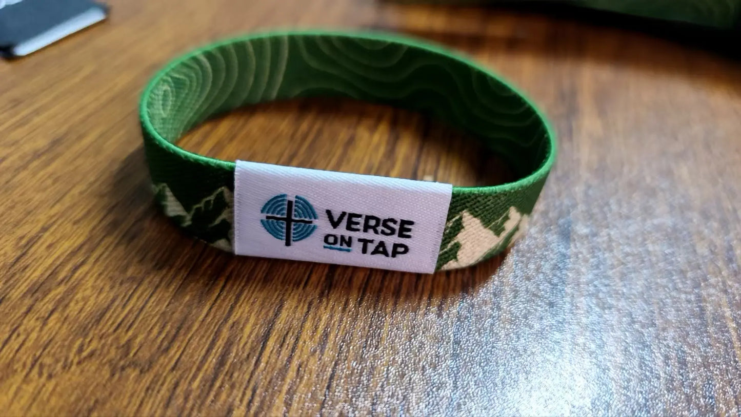 NFC wristband shown on table. Green wristband with mountain design and Verse On Tap label on a white background, reverse side has Topography lines.