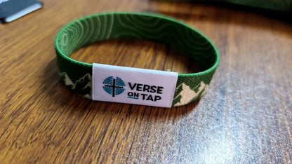 NFC wristband shown on table. Green wristband with mountain design and Verse On Tap label on a white background, reverse side has Topography lines.