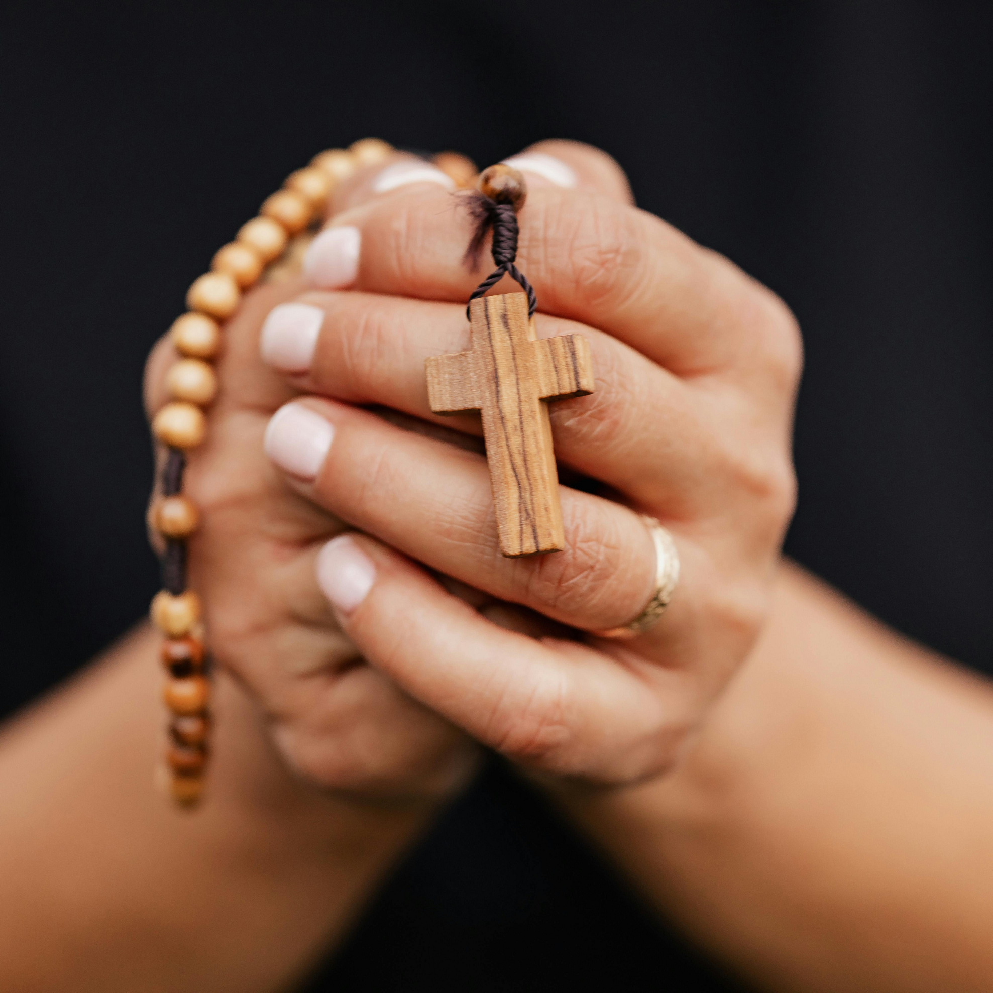 Hands holding a wooden cross attached to a rosary, symbolizing prayer, faith, and devotion.