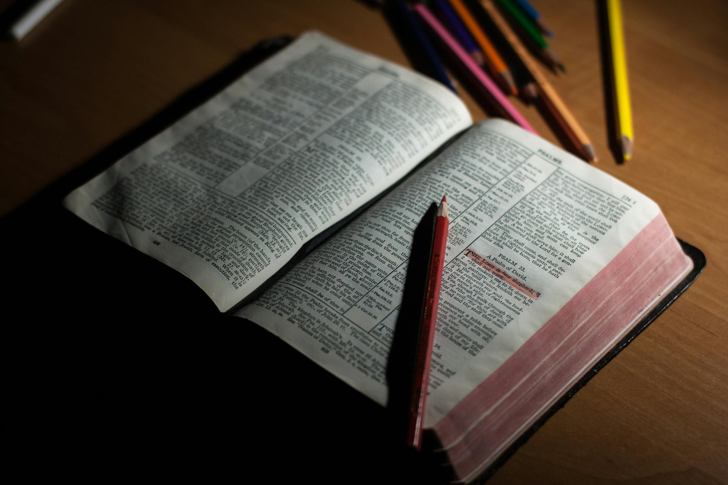 Open Bible on a wooden table with a pencil resting across the pages.