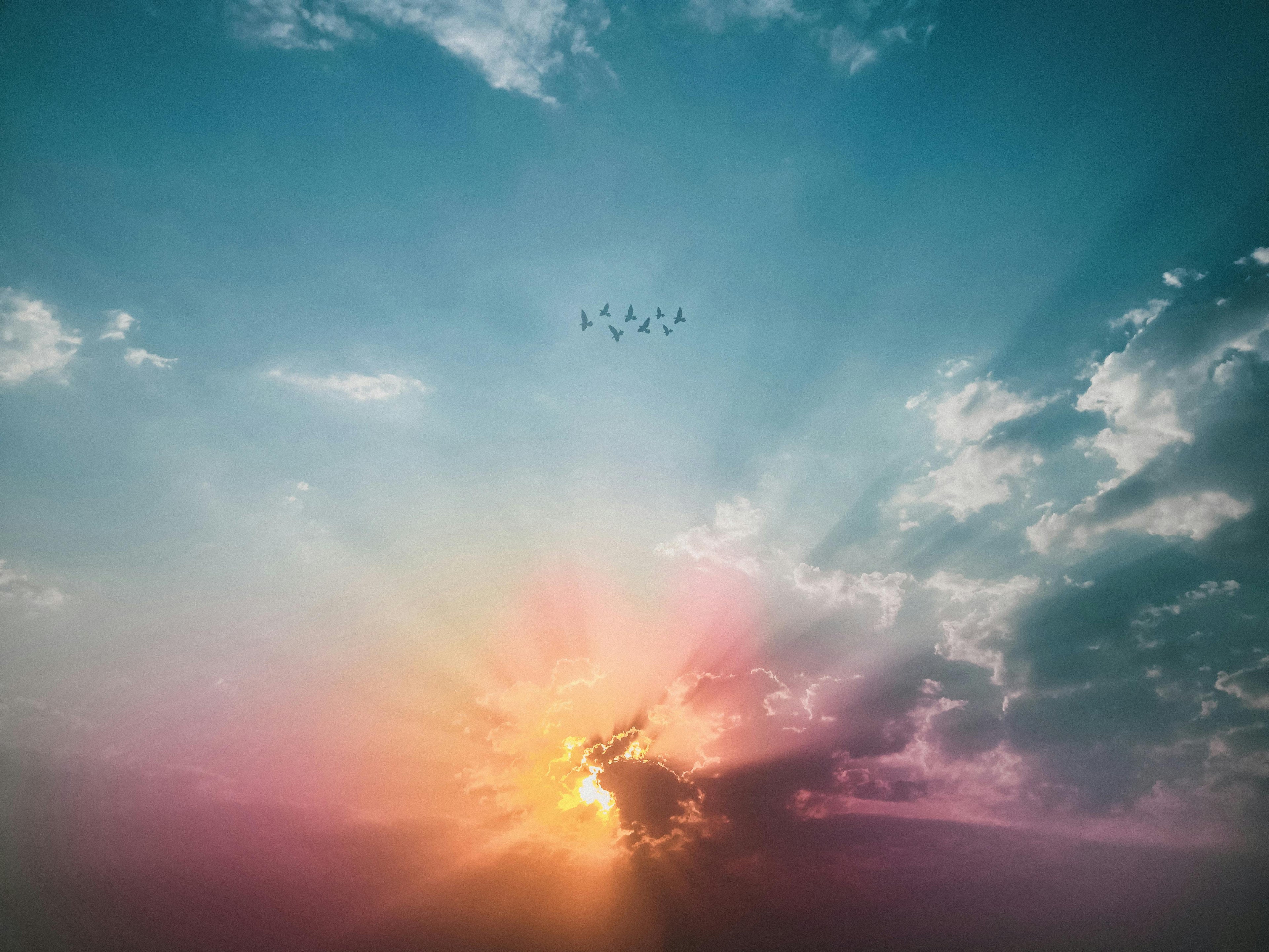 Sunlight breaking through colorful clouds at sunrise, with soft rays spreading across the sky and birds flying overhead.